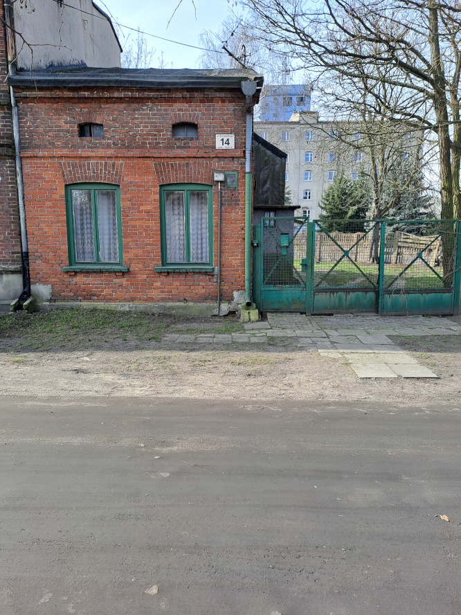 po lewej dom z czerwonej cegły, po prawej zielona stalowa brama