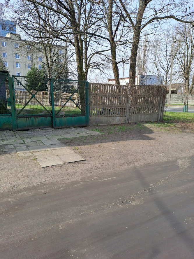 po lewej zielona stalowa brama, po prawej ogrodzenie betonowe