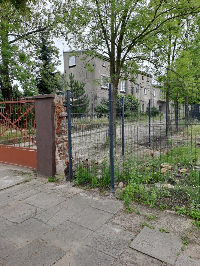 ogrodzony plac z budynkiem piętrowymw tle